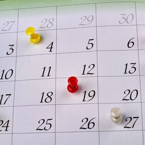 Many Colorful Push Pins On A Monthly Paper Calendar Page.